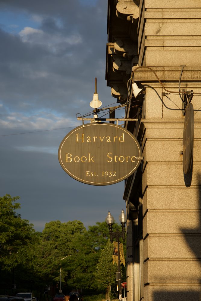 The round Harvard Book Store sign catching warm light against a cloudy sky.