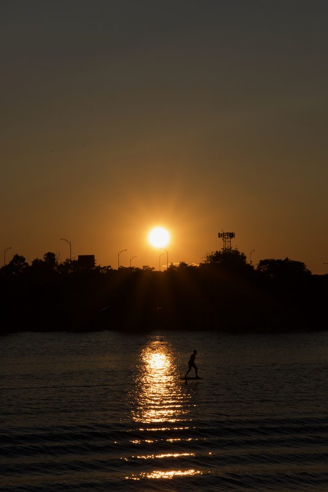 A paddleboarder silhouetted beside a trail of sunset light on the water.