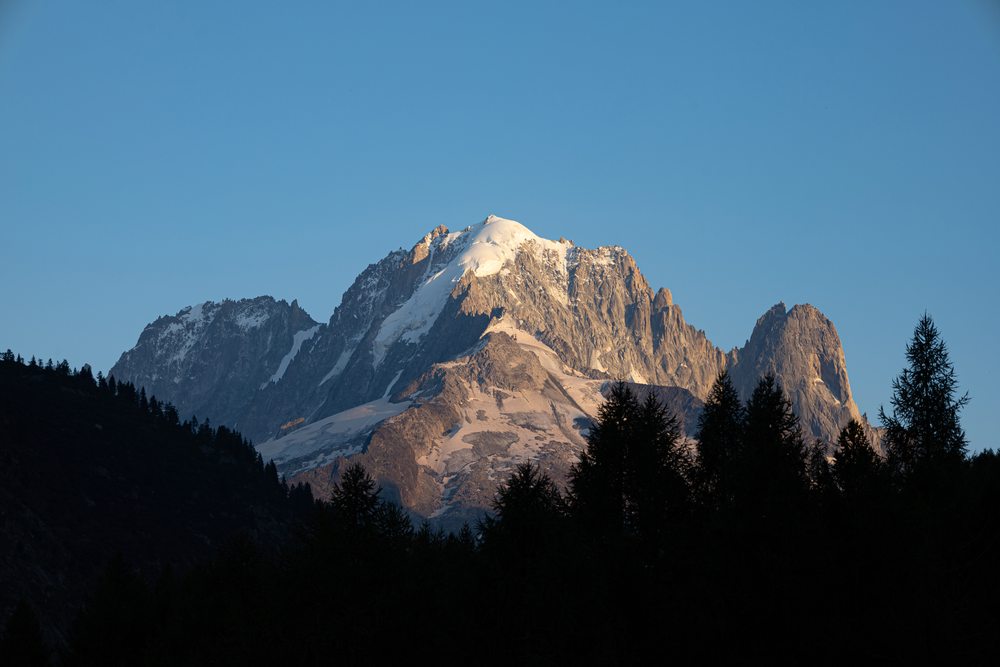 Warm evening light on a rocky summit framed by dark conifers.