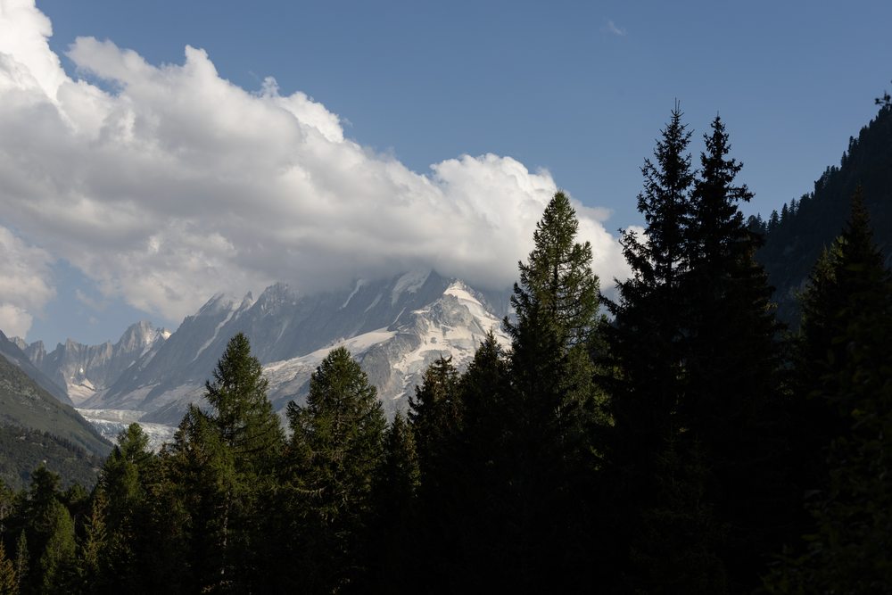Conifers frame mountain peaks beneath large white clouds.