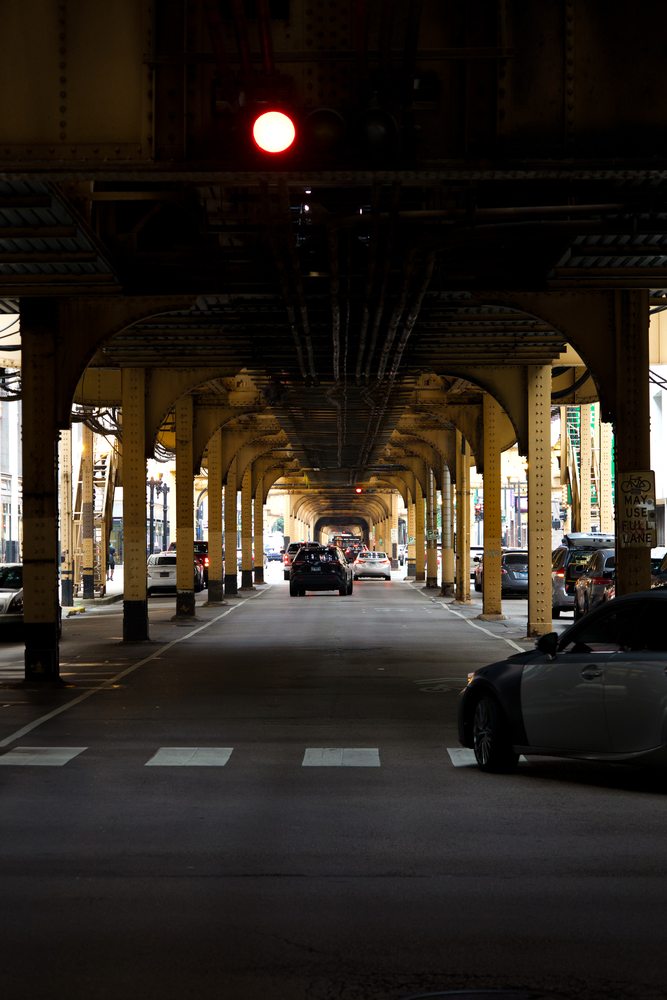 A red traffic light and repeating metal columns above a Chicago street.