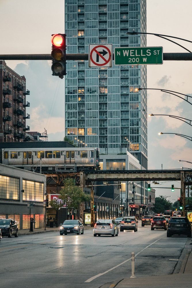 An elevated train crossing a city street lined with traffic lights and tall buildings.