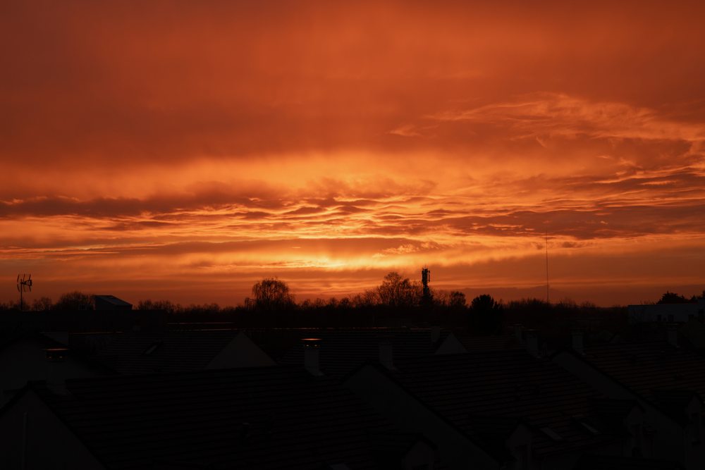 Layers of orange clouds over the dark silhouettes of rooftops.