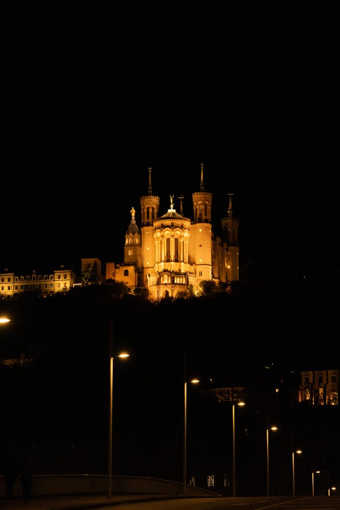 An illuminated basilica stands above the city at night, with street lamps below.