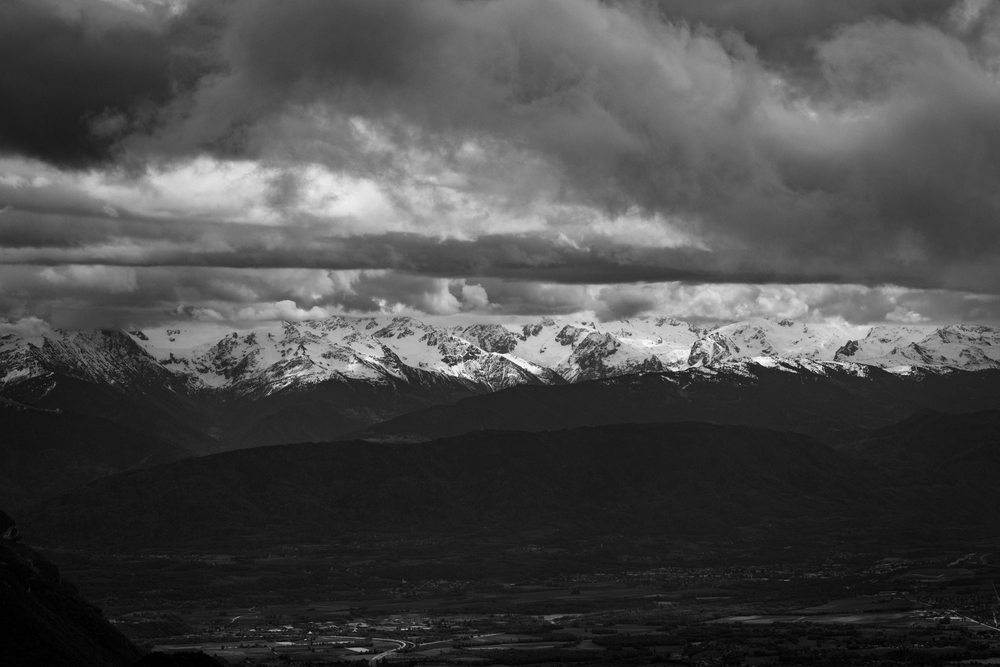 Snow-covered mountain ridges beneath dramatic clouds, photographed in black and white.