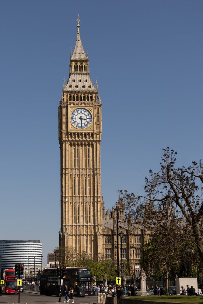 Elizabeth Tower rises above buses and pedestrians under a clear blue sky.