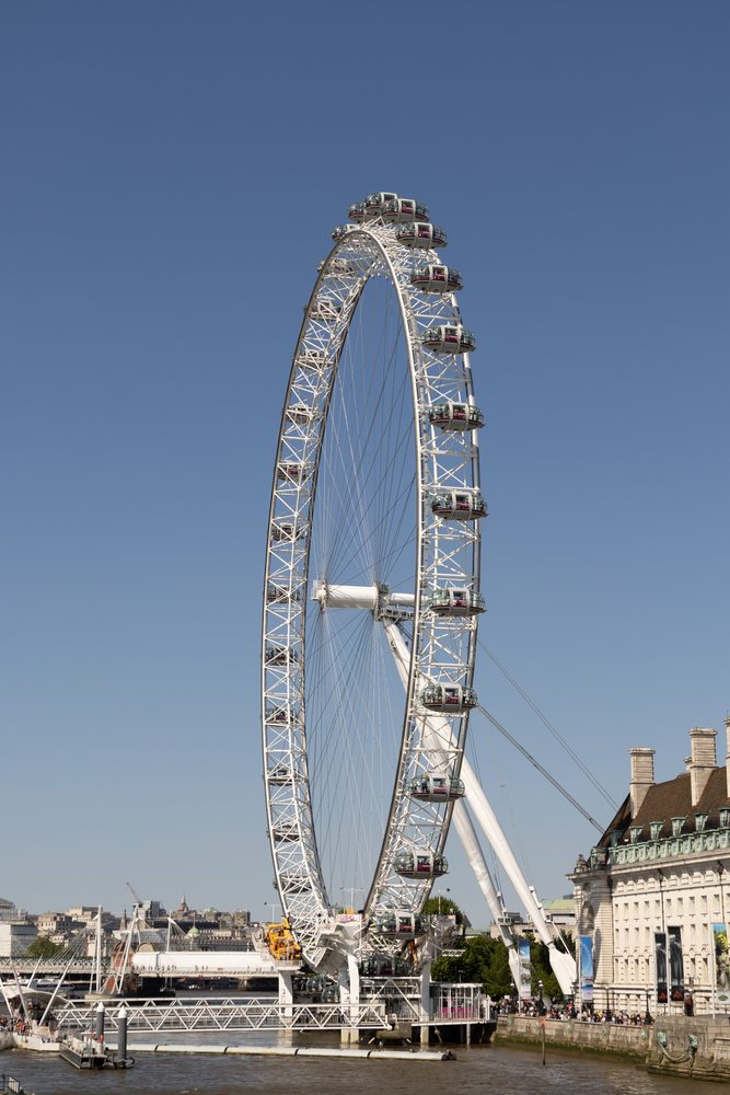 The London Eye and its passenger capsules above the Thames beneath a clear blue sky.