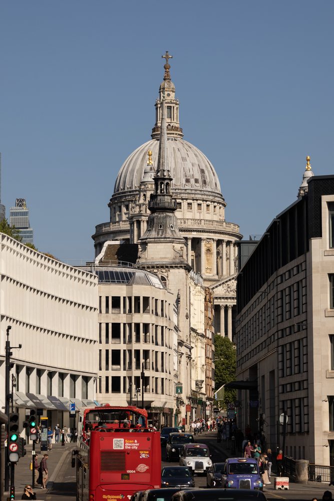 The dome of St Paul’s Cathedral above a busy street with a red bus, taxis and pedestrians.