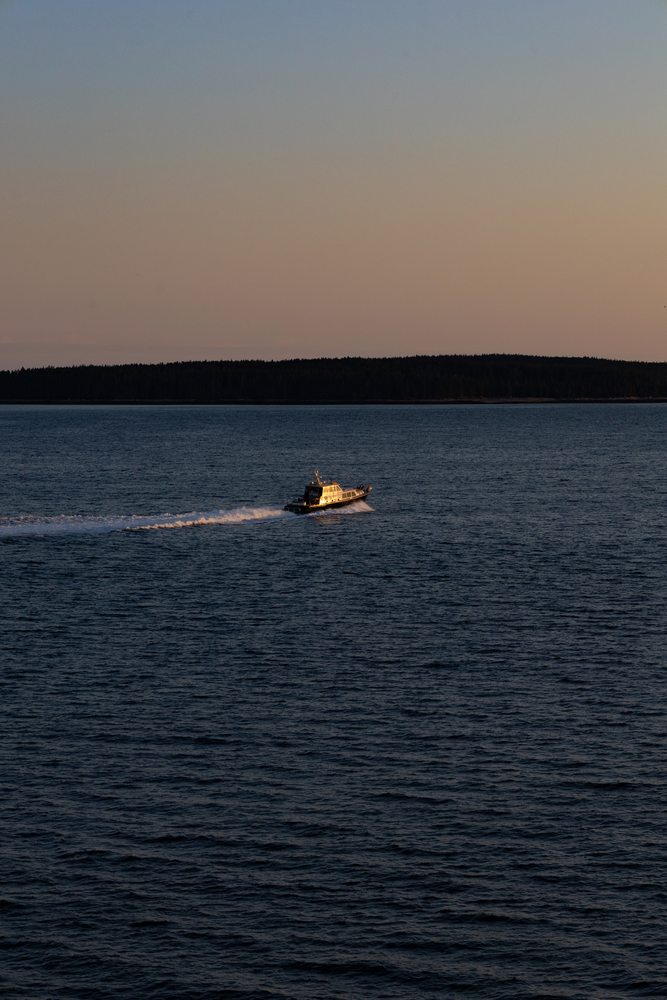 A small motorboat and its wake crossing dark water at dusk.