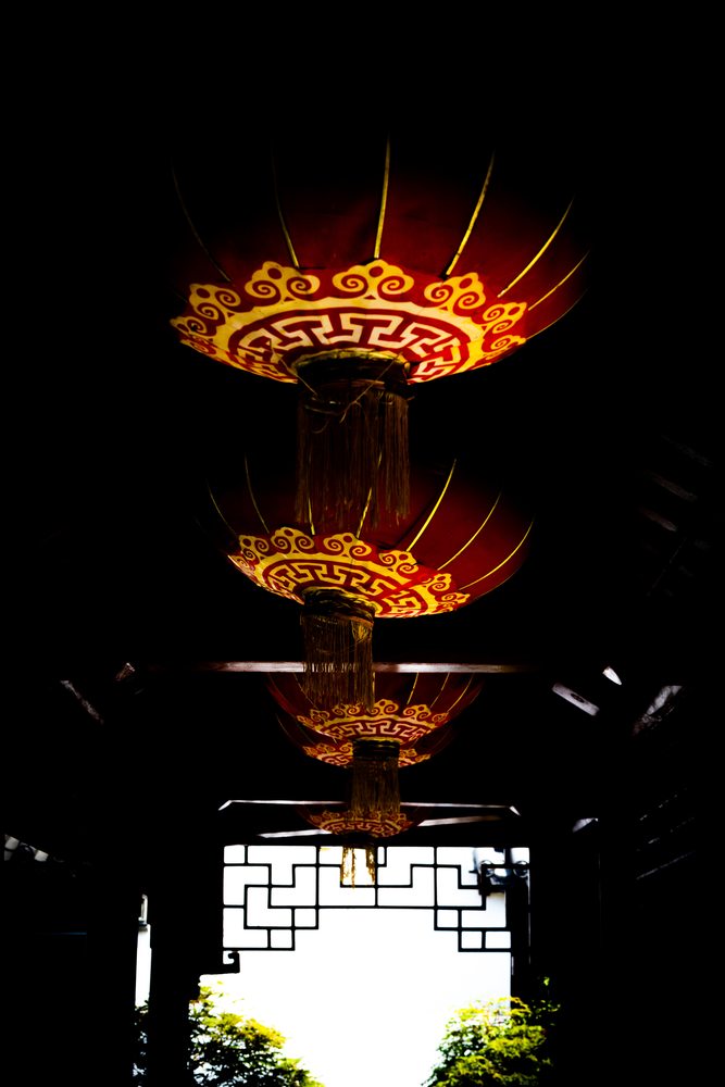 Red and gold lanterns hanging in a dark interior above a bright doorway.