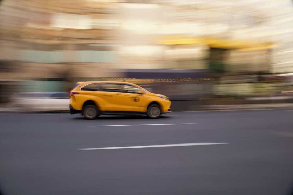 A yellow taxi photographed against blurred buildings in a panning shot.