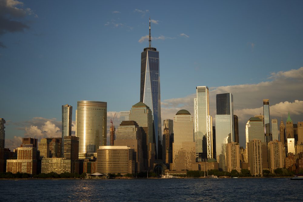 Waterfront buildings catch warm evening light beneath a tall tower and scattered clouds.