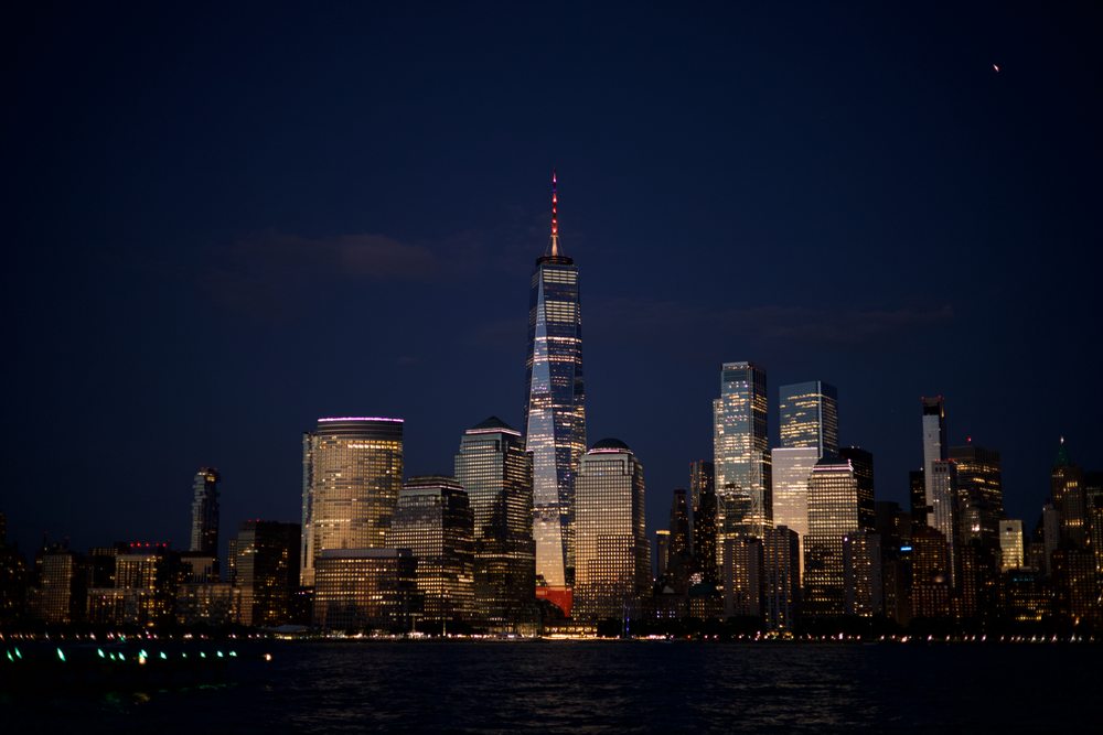 Illuminated towers on the Manhattan waterfront beneath a deep blue sky.