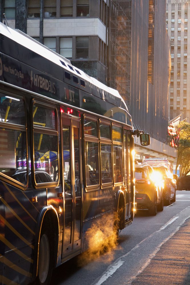 A city bus and rising steam catching golden light on a New York street.